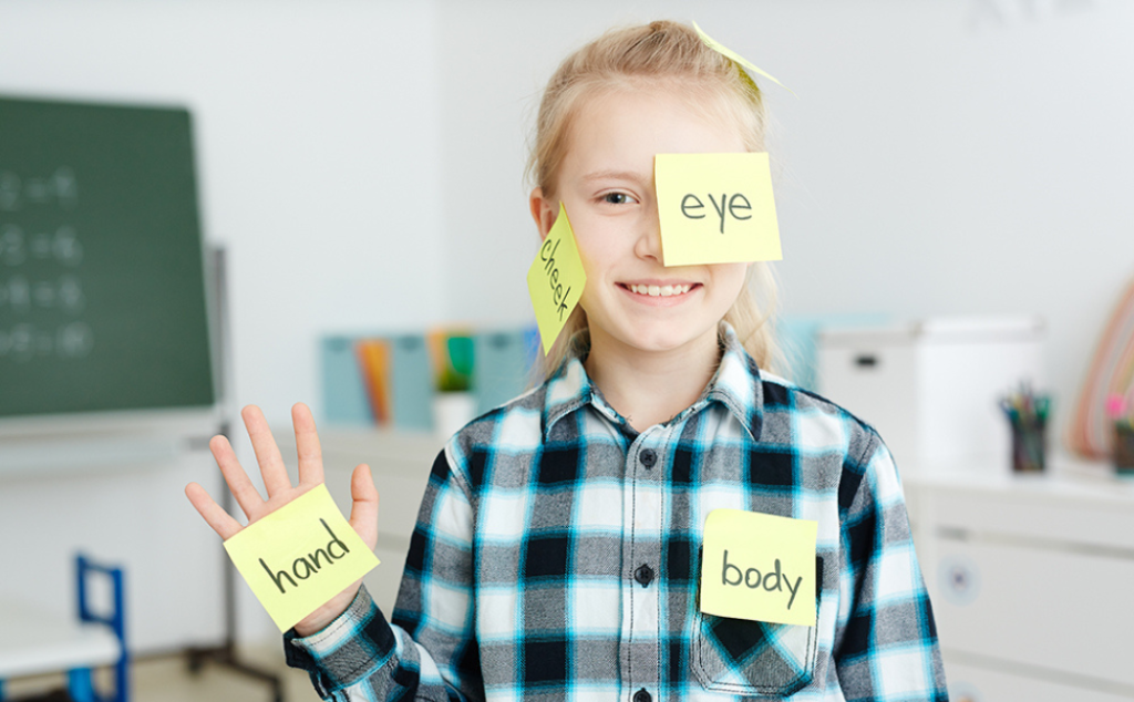 Criança sorrindo com papéis escrito palavras em inglês