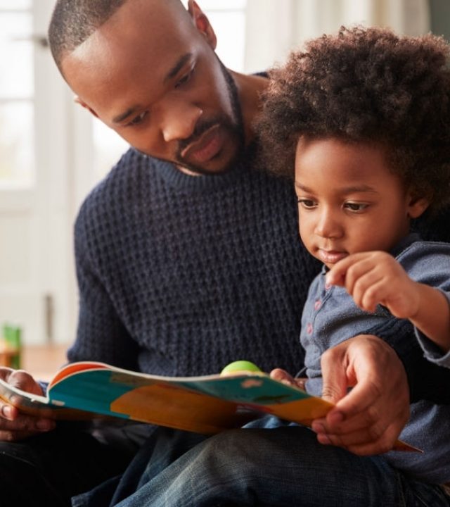 Father And Young Son Reading Book Together At Home
